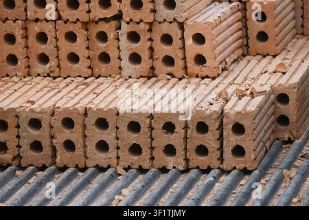 A stacked hollow clay bricks on corrugated metal surface, earthy texture and repetitive pattern conveying construction readiness and rustic warmth Stock Photo