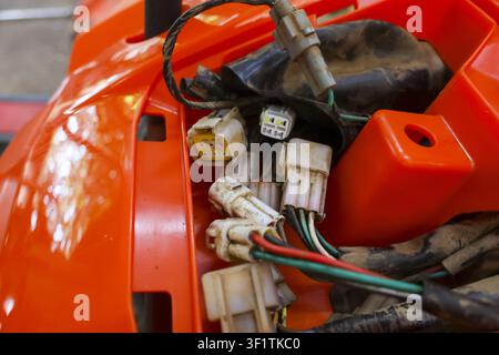 A wiring harness and plastic connector cluster on orange motorcycle fairing, close up showing dirt, insulation and colored wires with gritty workshop Stock Photo