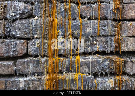 A worn brick wall with dripping wax layers in gray and amber tones creating textured vertical streaks and gritty urban decay atmosphere Stock Photo