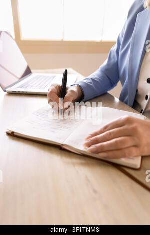 Professional woman writing information in notebook at office desk, closeup Stock Photo
