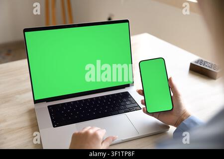 Woman using smartphone and laptop with green blank mockup screens Stock Photo