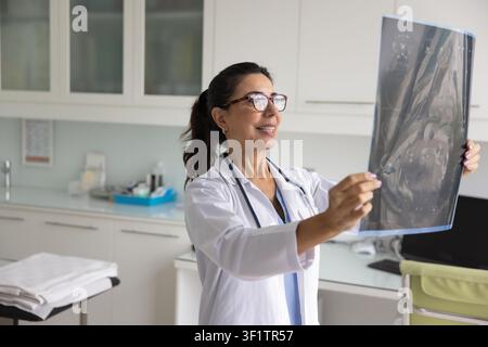 Positive satisfied successful mature doctor woman looking at X-ray image Stock Photo
