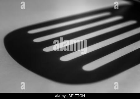 Kitchen spatula silhouette casting striped light pattern in monotone Stock Photo