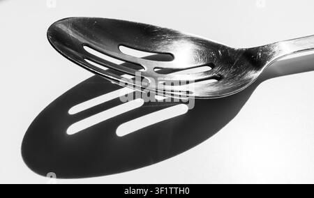Slotted spoon casting striped shadow on surface in black and white Stock Photo