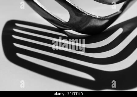 Slotted spatula edge casting curved striped shadow in black and white Stock Photo