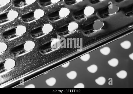 Grater blade edge with punched holes casting circular shadow in black and white Stock Photo