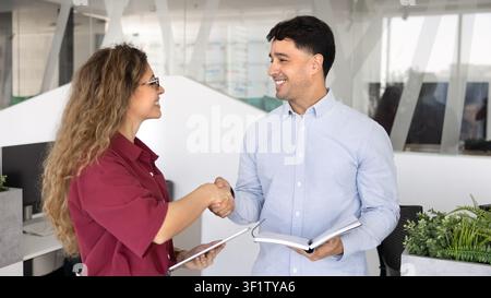 Colleagues greeting, shaking hands standing in corporate office Stock Photo