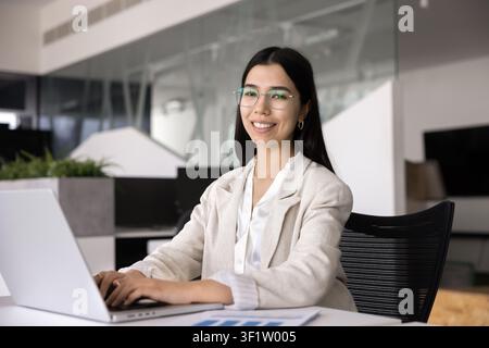 Smiling young businesswoman using laptop at desk, portrait Stock Photo