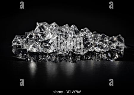 Pile of clear crushed ice cubes with reflection on black background, close up. Heap of shiny transparent acrylic ice cubes reflecting on dark glossy s Stock Photo