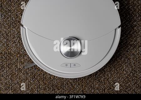 White robot vacuum cleaner top view on carpet, close up. Smart robotic vacuum cleaner on home carpet with lidar sensor and control buttons. Modern dom Stock Photo