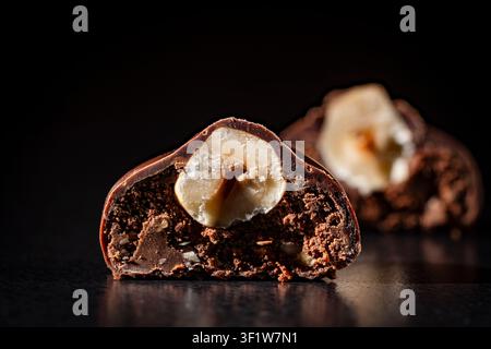 Chocolate truffle with whole hazelnut filling, close up. Macro of chocolate truffle cut in half revealing whole hazelnut and creamy filling. Premium h Stock Photo