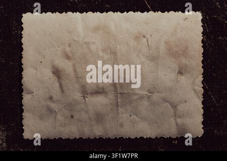 Blank vintage photo frame with wavy edges on dark background, close up. Top view of an empty old textured paper card with scalloped edges isolated on Stock Photo