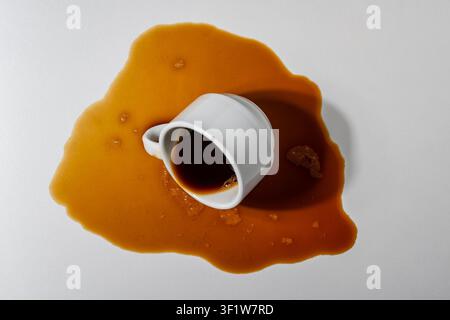 Spilled coffee from overturned white cup on light background, close up. Top view of a spilled puddle of dark espresso coffee with a fallen white ceram Stock Photo