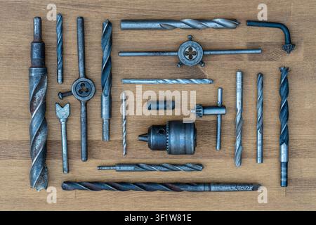 Old rusty drills and dies on the wooden table background, close up, top view. Dirty set old working vintage tools Stock Photo