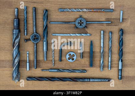 Old rusty drills and dies on the wooden table background, close up, top view. Dirty set old working vintage tools Stock Photo