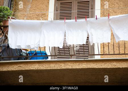 white sheets drying on a clothesline on a balcony with brown shutters and textured wall, everyday domestic scene from below the balcony period period Stock Photo