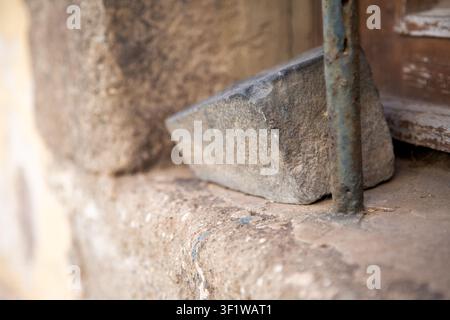 doorstop resting against a brick wall in a neutral, everyday outdoor residential setting with a close-up perspective and concrete, brick, and metal Stock Photo