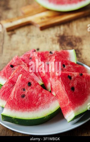 Slices of ripe red watermelon with black seeds served on a plate on a rustic wooden background. Stock Photo