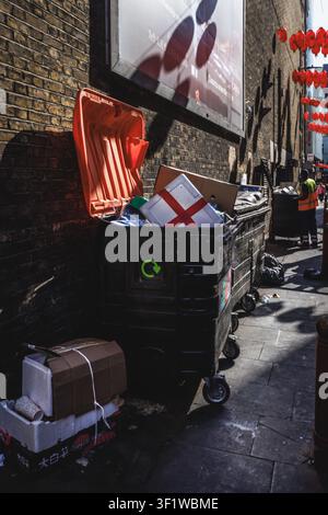 A discarded St George's Cross flag in a large rubbish bin beneath traditional Chinese street lanterns in London's Chinatown after the World Cup. Stock Photo