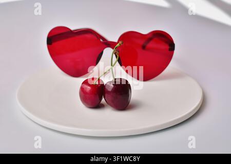 A pair of cherries in front of red heart-shaped sunglasses, love concept background Stock Photo