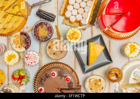An overhead shot of a dessert feast featuring chocolate cake, fruit pies, red gelatin, and various creamy treats on a wooden table. Stock Photo
