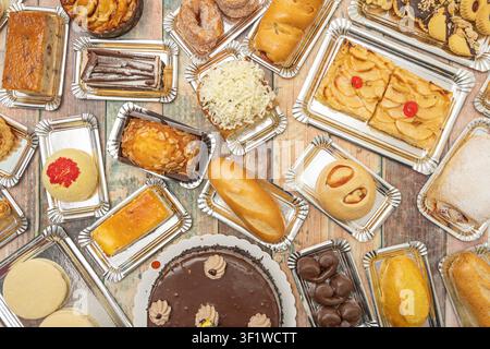 Overhead view of various pastries, cakes, and breads including apple tart and chocolate cake on silver trays on a wooden table. Stock Photo