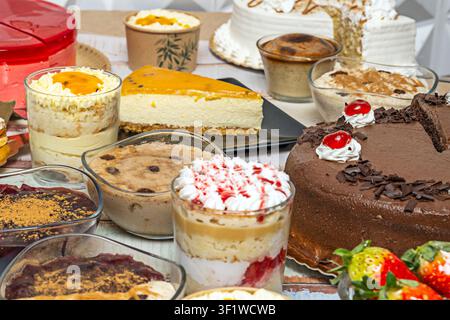 Close-up of assorted desserts featuring a rich chocolate cake with cherries, cheesecake slice, layered parfaits, and various creamy puddings in glass Stock Photo