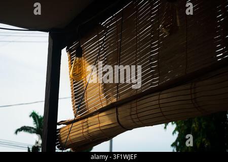 Sunlight shining through partially rolled bamboo blinds on a veranda, creating natural light and shadow patterns in a tropical residential setting. Stock Photo