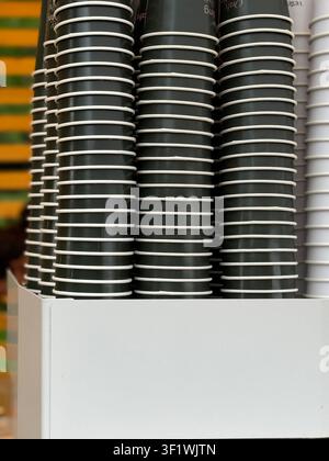 Stacks of disposable coffee cups in holder against colorful striped wall, available as background. Mobile photo Stock Photo