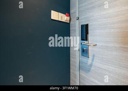 Hotel key card power switch beside digital door lock, room access shows a guest inserting a key card into the wall slot to activate electricity and in Stock Photo