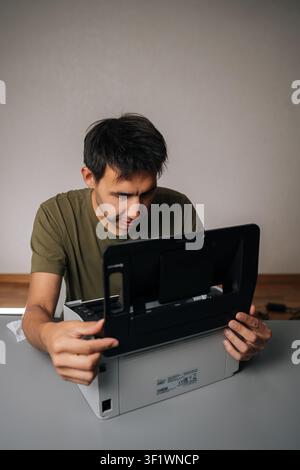 Top view of technician examining components of disassembled laser printer, troubleshooting and performing maintenance in workshop environment Stock Photo