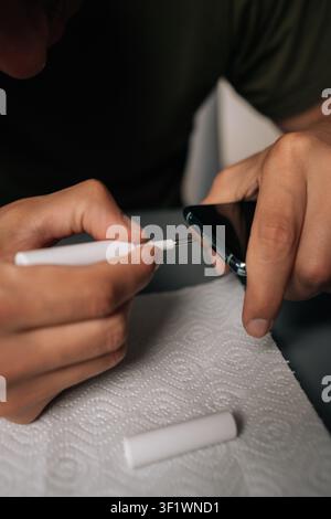 Vertical cropped shot of technician cleaning smartphone using specialized tools sitting at table, ensuring optimal quality and device performance. Stock Photo