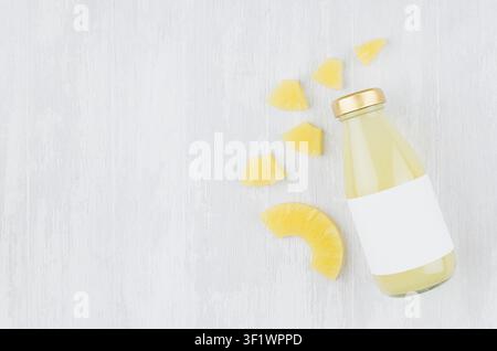 Bright pinapple yellow juice in glass bottle with blank label, sliced fruit on white wooden board, top view, copy space, template for design, advertising, portfolio. Stock Photo