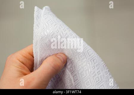 A man's hand in the frame holds a triangular white napkin on a blurred background. Kitchen textiles, selective focus. Stock Photo