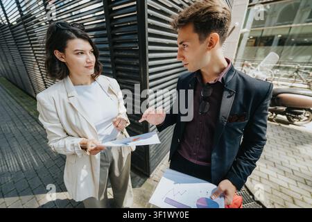 Business colleagues discussing charts and reports during an outdoor meeting by a modern office building Stock Photo