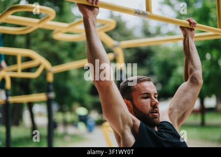 Athletic man doing pull-ups on outdoor yellow bars during a strength workout in a park Stock Photo