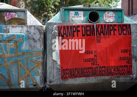 Berlin, Germany - July 16, 2026: Anti-AI and anti-surveillance demonstration posters on a glass recycling bin in Kreuzberg. Stock Photo