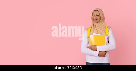 Black Muslim female student in hijab holding notebooks and looking aside Stock Photo