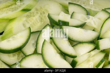 Cucumber cuts and slices in white bowl close up. Green vegetable cuts for salad isolated, healthy natural plant pieces, macro cucumbers slicing on whi Stock Photo