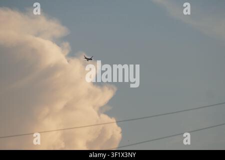 Silhouette of a passenger airplane flying past a massive, sunlit cumulus cloud formation in a dramatic blue sky. Concept for aviation travel. Stock Photo
