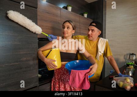 Cozy home routine, teamwork, and domestic chores. Young couple cleaning their apartment together, dusting and wiping surfaces. Stock Photo