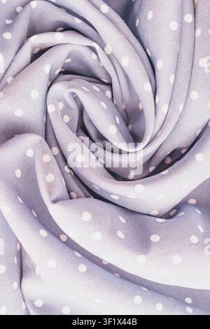 Vertical close up shot of a soft lavender purple polka dot fabric material texture twisted into a beautiful spiral rose pattern on a cozy comfortable Stock Photo