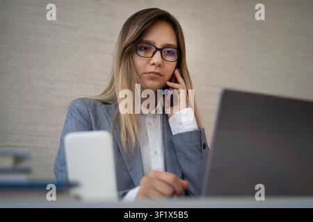 Businessman multitasking on a phone call while reaching for papers and a pen at his office desk. High workload and busy day. the man is talking on two Stock Photo