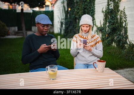 Two friends using smartphones sitting at a table outdoors Stock Photo