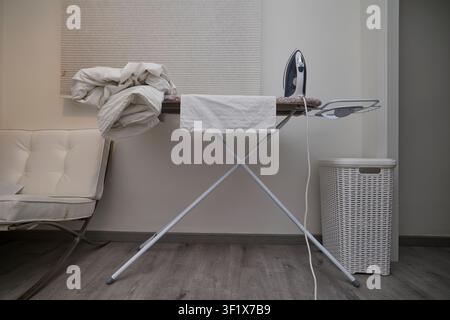 Ironing clothes on ironing board in modern home interior with laundry basket. Stock Photo