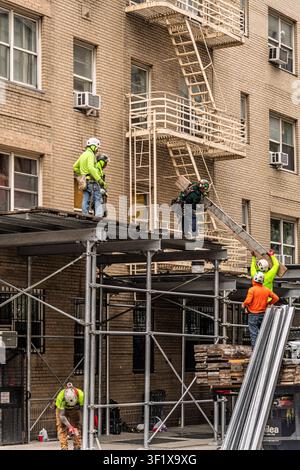 Construction workers on scaffolding perform building maintenance and repairs on an apartment building in Manhattan, New York. Stock Photo