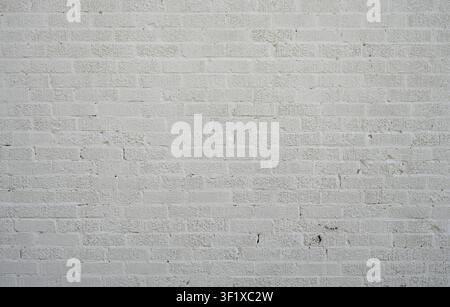 Horizontal close up of painted white brick wall with rough uneven bricks, cracked mortar, patched holes Stock Photo