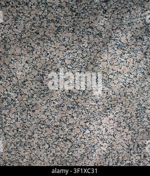 Vertical close up of a polished beige granite surface with multicolor blotches, scattered specks, soft sun rays Stock Photo