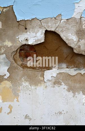 Vertical close up of a weatherworn multilayer wall showing cracked painted concrete, exposed terra cotta clay Stock Photo