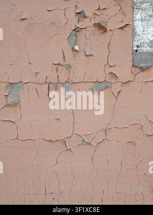 Vertical close up of a weatherworn tan painted wall surface with large cracked peeling paint patches revealing white painted concrete Stock Photo